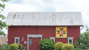 Un granero rojo con techo metálico desgastado, un letrero que dice "Freeman Barn" y una decoración de colcha colorida.
