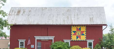 Une grange rouge avec un toit en métal usé par les intempéries, une enseigne indiquant « Grange Freeman », et une décoration colorée en forme de patchwork.
