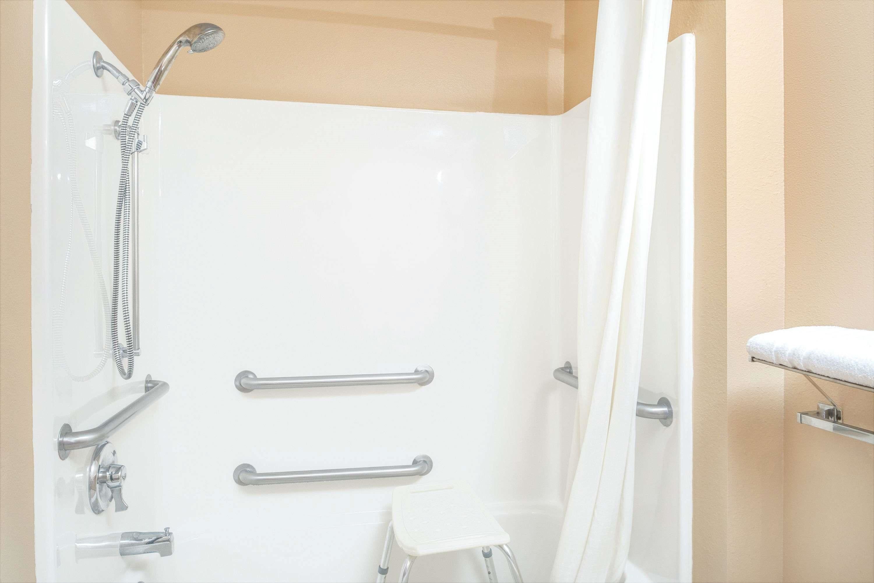 A modern bathroom with a walk-in shower, grab bars, and a white towel rack.