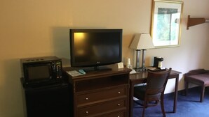 Una habitación de hotel con un escritorio de madera, televisión, lámpara, silla y microondas.