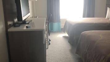 A hotel room with a desk, a television, two beds, a window with curtains, and a carpeted floor.