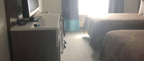 Quarto de hotel com escrivaninha, televisão, duas camas, janela com cortinas e chão coberto de carpete.