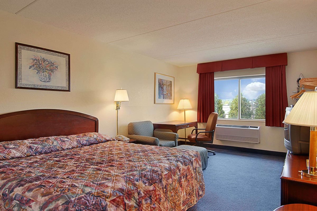 Hotelkamer met een bed, bureau, stoel, twee lampen, een televisie en een raam met gordijnen.
