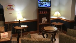 Vestíbulo de hotel con un cartel de desayuno Superstart, un televisor mostrando un noticiero y una zona de estar con dos mesas y sillas.