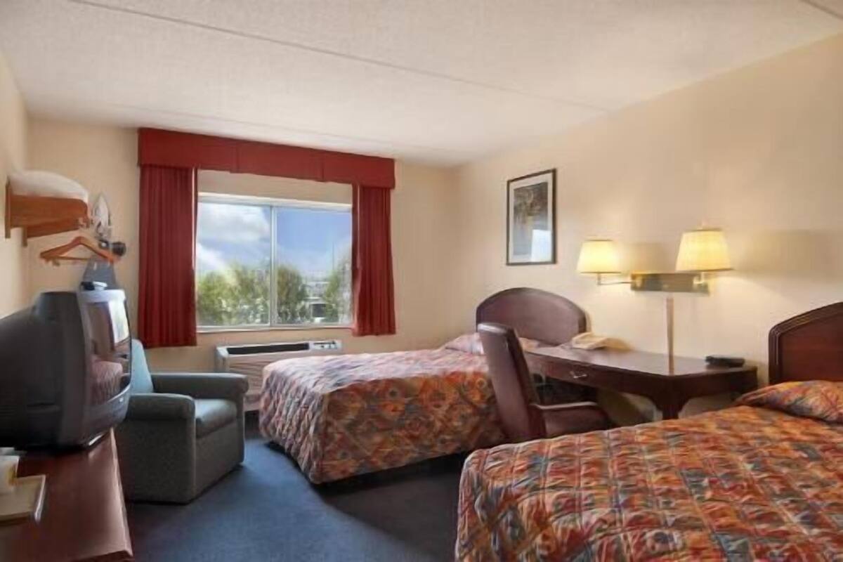 Een hotelkamer met twee bedden, een bureau met lamp, een stoel, een televisie en een raam met gordijnen.