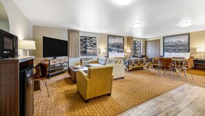 A hotel room with a flat-screen TV, a sofa, a dining table with chairs, and artwork on the walls. - Super 8 by Wyndham Cody (Cody)