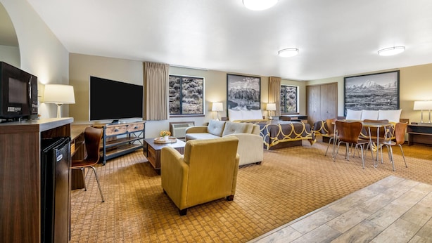 A hotel room with a flat-screen TV, a sofa, a dining table with chairs, and artwork on the walls. - Super 8 by Wyndham Cody (Cody)