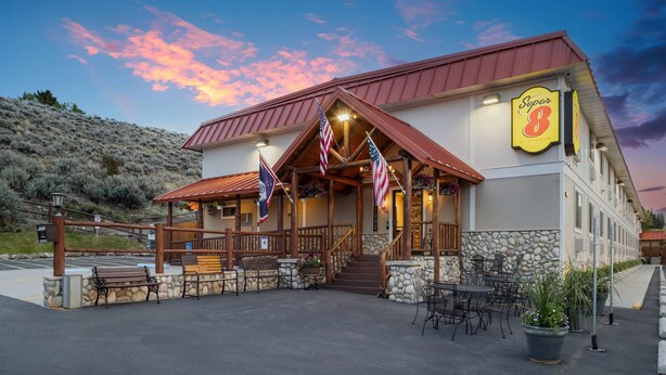A Super 8 motel with a stone facade, outdoor seating, and American flags. - Super 8 by Wyndham Cody (Cody)