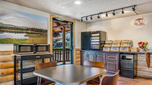 A breakfast area with a table, chairs, a refrigerator, a microwave, and a view of a lake through an open door. - Super 8 by Wyndham Cody (Cody)