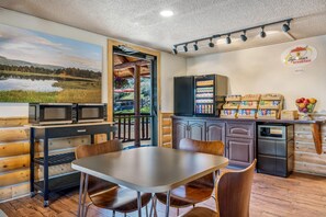 A breakfast area with a table, chairs, a refrigerator, a microwave, and a view of a lake through an open door. - Super 8 by Wyndham Cody (Cody)