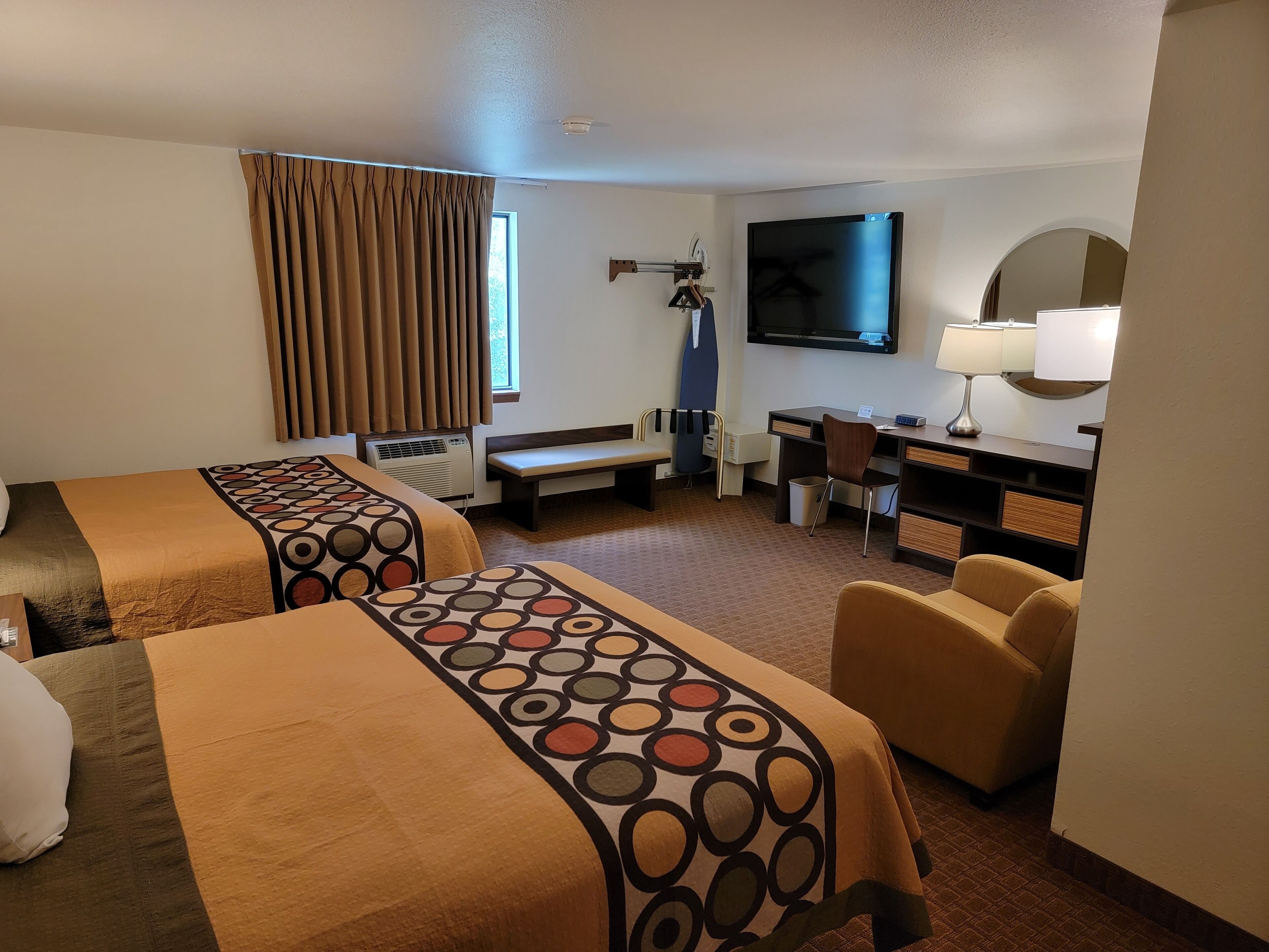 A hotel room with two beds, a desk, a chair, a television, and a lamp.
