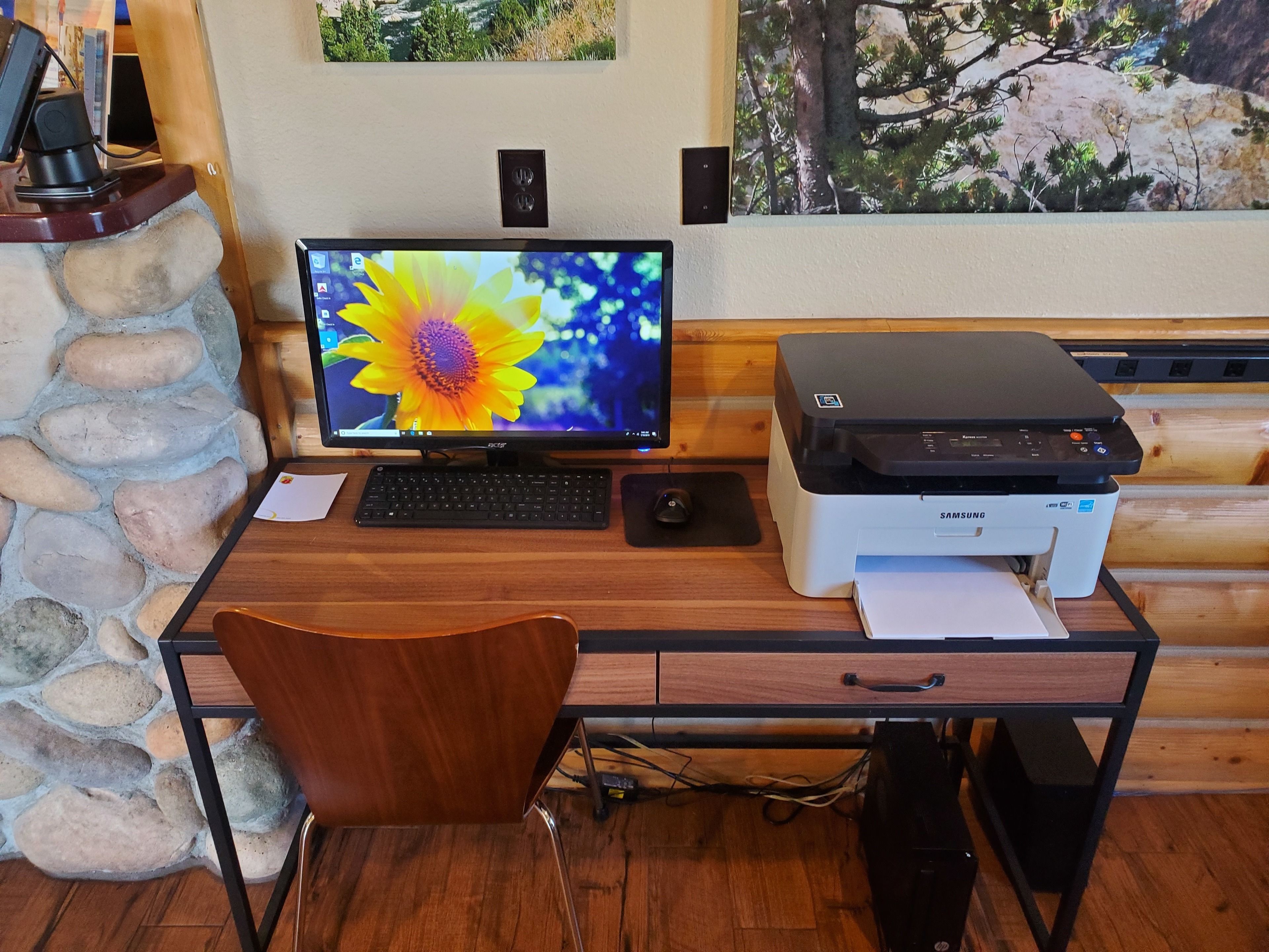 A wooden desk with a computer monitor, keyboard, mouse, and a Samsung printer.