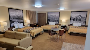 A hotel room with two beds, a sofa, a table, and chairs. There are large framed pictures on the walls. - Super 8 by Wyndham Cody (Cody)
