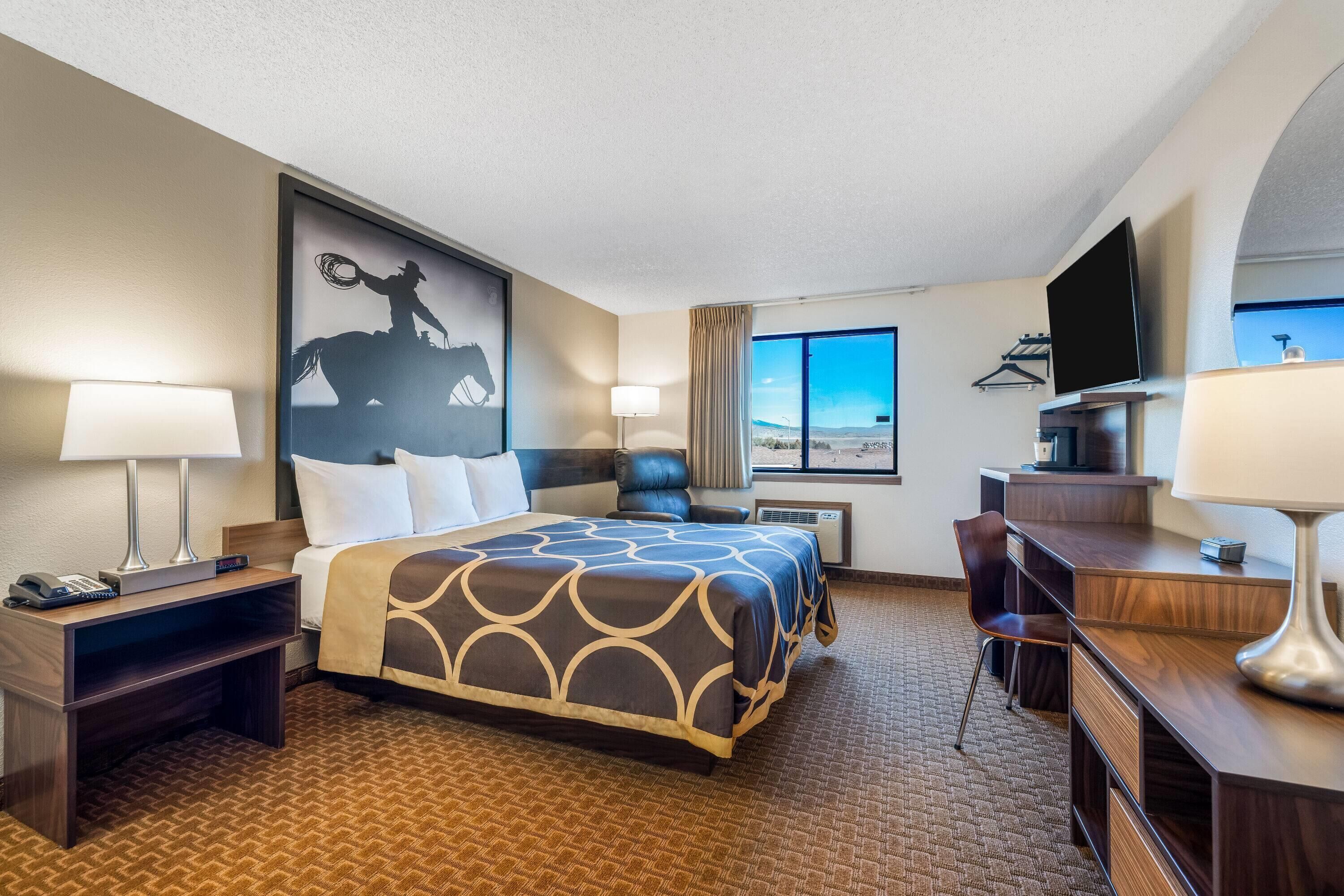 Une chambre d’hôtel avec un grand lit, un bureau, une chaise, une télévision et un tableau représentant un cow-boy à cheval.