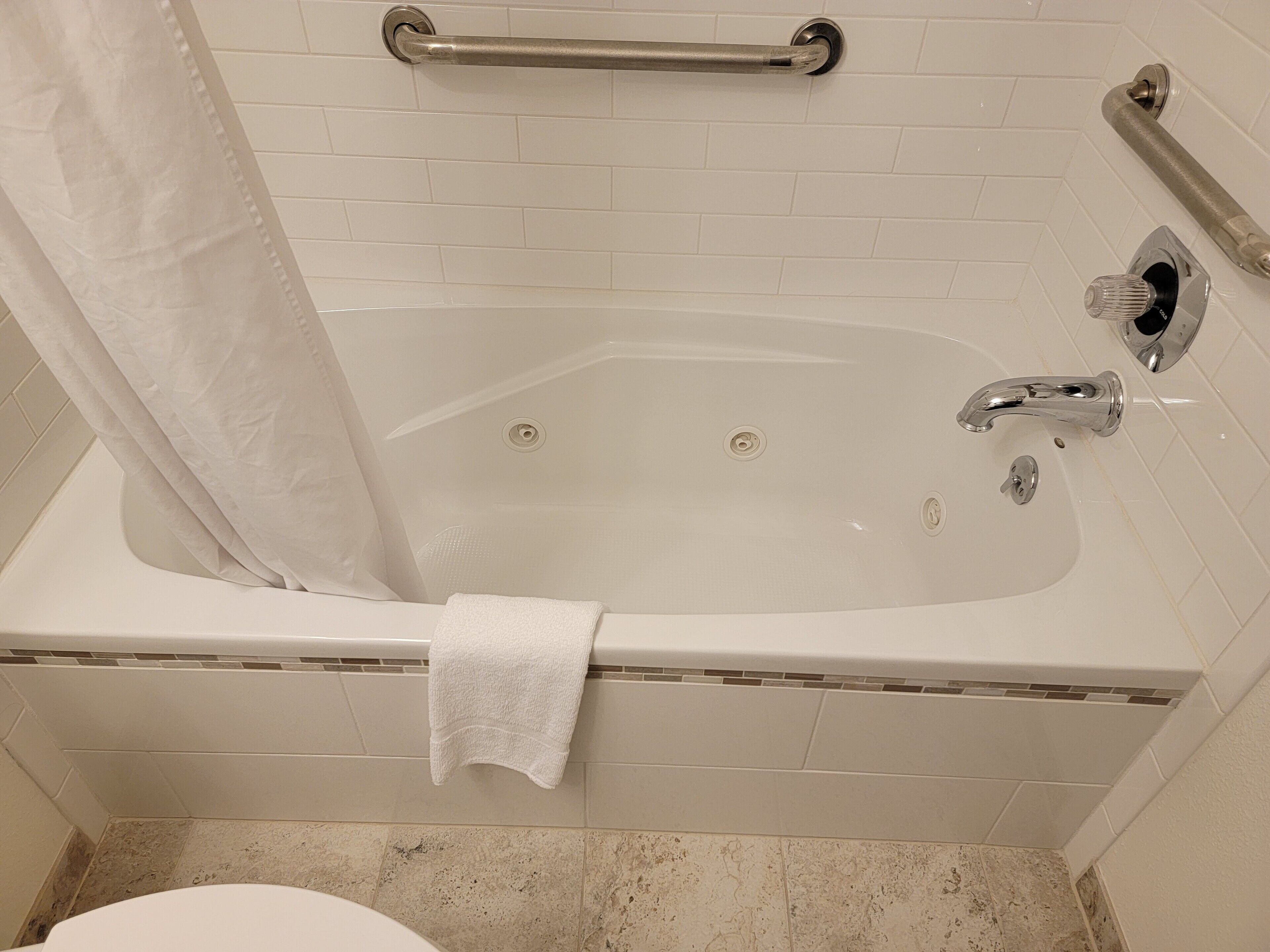 A bathroom with a bathtub, a shower curtain, a grab bar, and a towel.