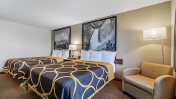 A hotel room with two beds, a chair, a lamp, and two large wall-mounted pictures.