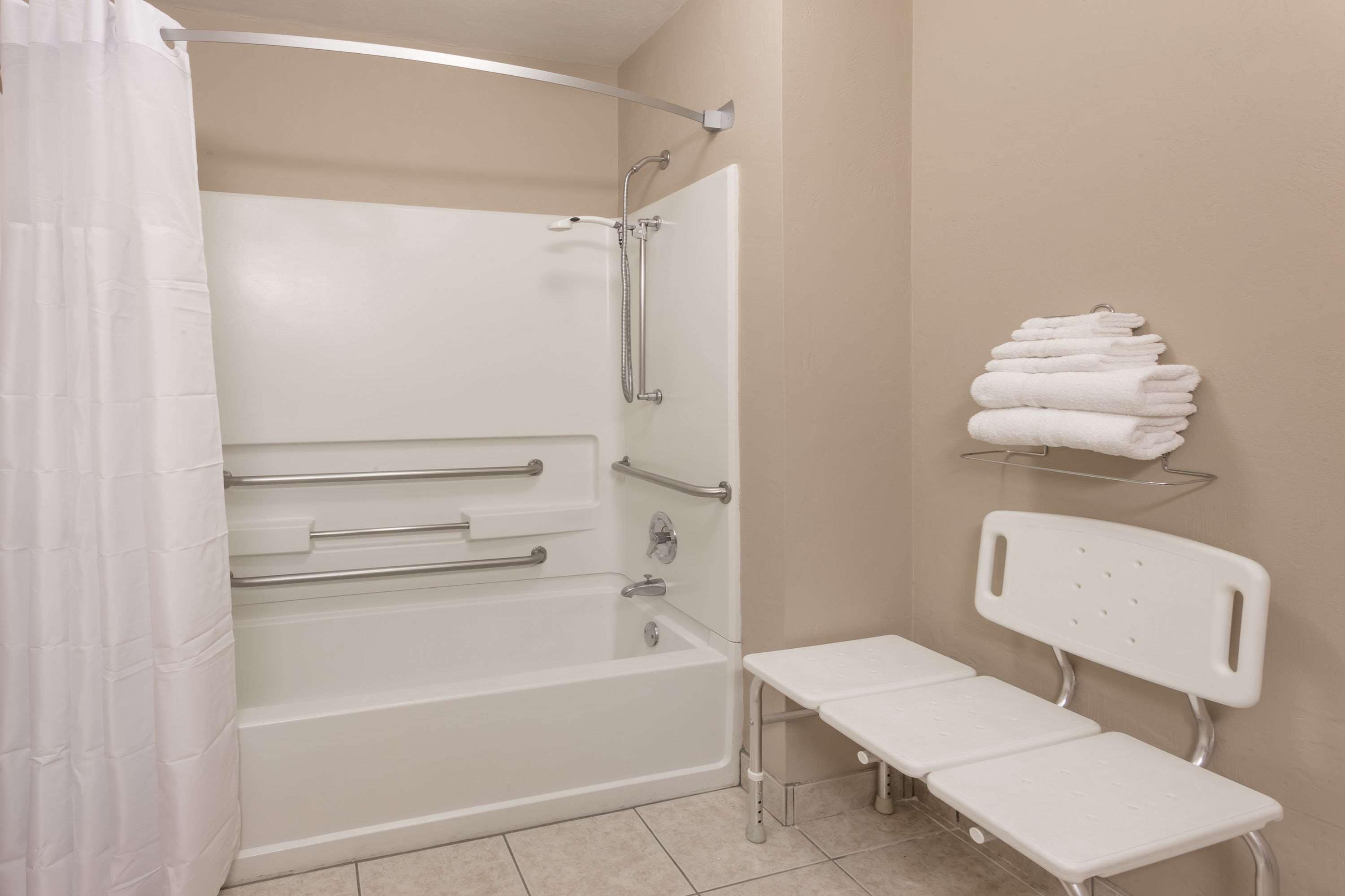 A bathroom with a bathtub, a shower, a bench, and a shelf with towels.