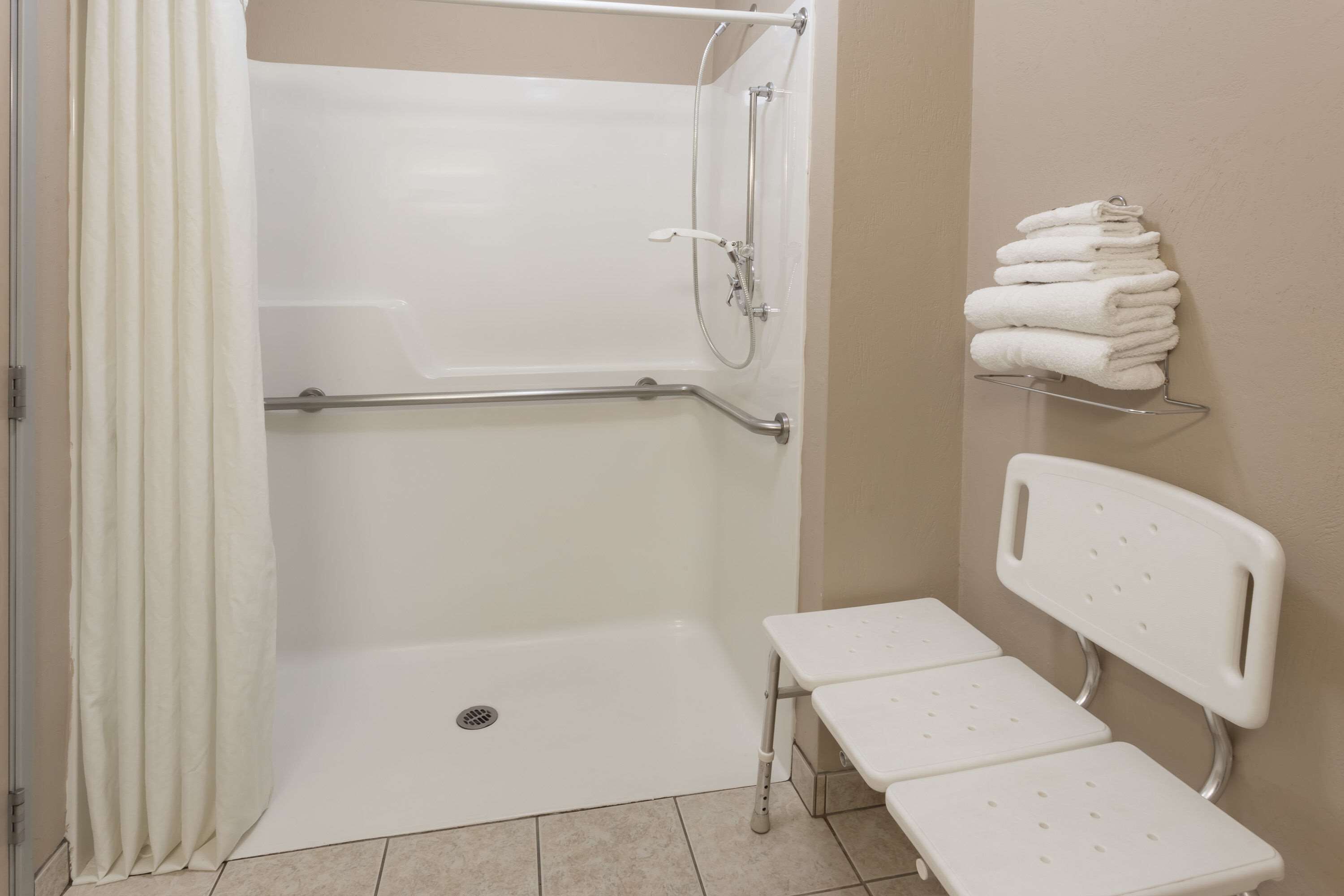 A bathroom with a shower, a grab bar, a bench, and a towel rack.
