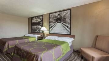 Habitación de hotel con dos camas, una silla, una mesita de noche y dos cuadros colgados en la pared.