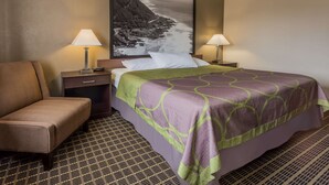 A hotel room with a bed, a chair, a nightstand, a lamp, and a large framed picture on the wall. - Super 8 by Wyndham Corvallis (Corvallis)