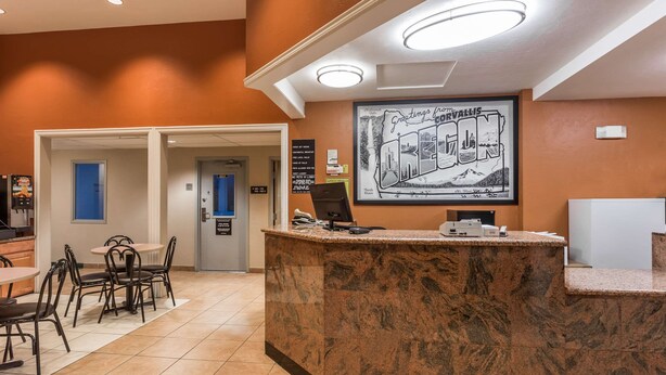 A hotel reception area with a marble counter, a framed welcome sign, and a dining area with chairs and tables. - Super 8 by Wyndham Corvallis (Corvallis)