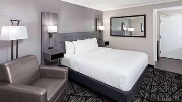 A modern hotel room with a large bed, a sofa, a nightstand, a wall-mounted lamp, and a mirror.