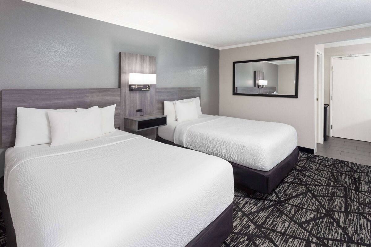 A hotel room with two beds, a nightstand, a lamp, a mirror, and a patterned carpet.