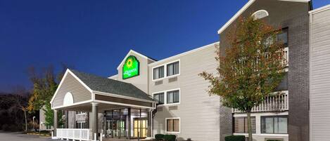 A hotel with a prominent 'Quinta' sign, a covered entrance, and a landscaped area with a tree.