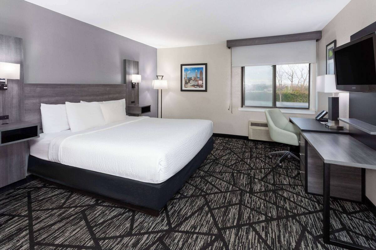 A hotel room with a large bed, a desk, a chair, a TV, and a window with a view.