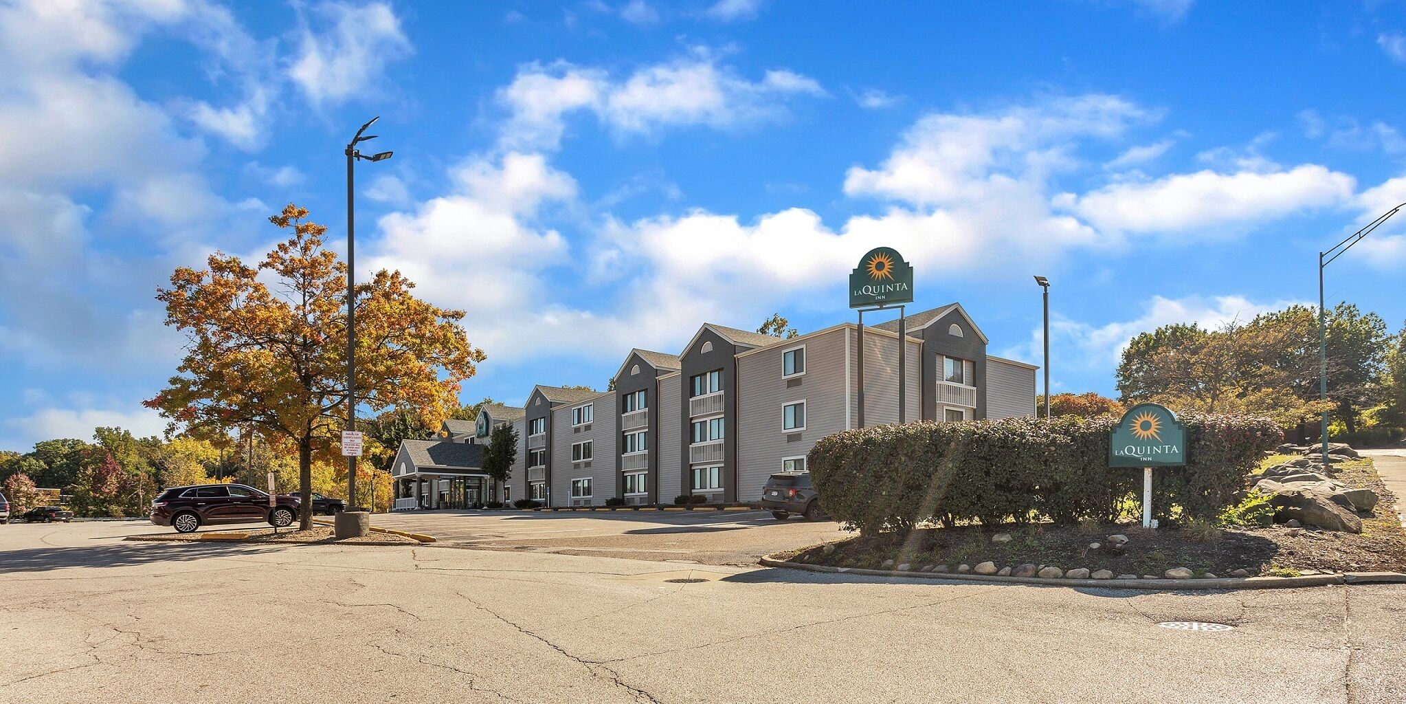 A multi-story hotel with a central entrance, a parking lot, and a clear sky.