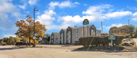 A multi-story hotel with a central entrance, a parking lot, and a clear sky.