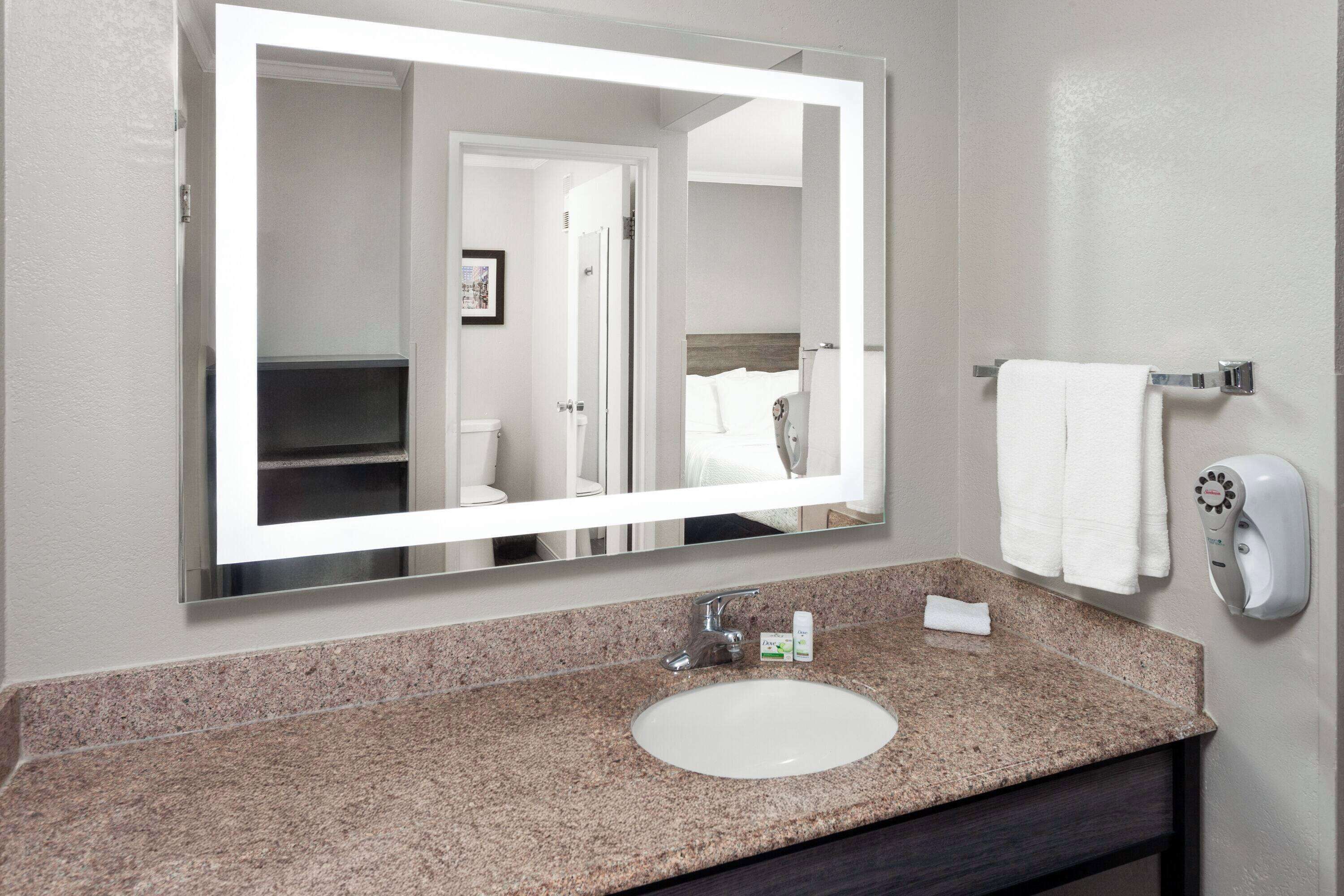 A bathroom with a granite countertop sink, a large mirror, a towel rack, and a hand dryer.