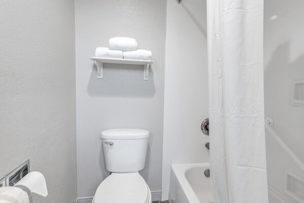A bathroom with a toilet, a shelf with towels, and a bathtub.