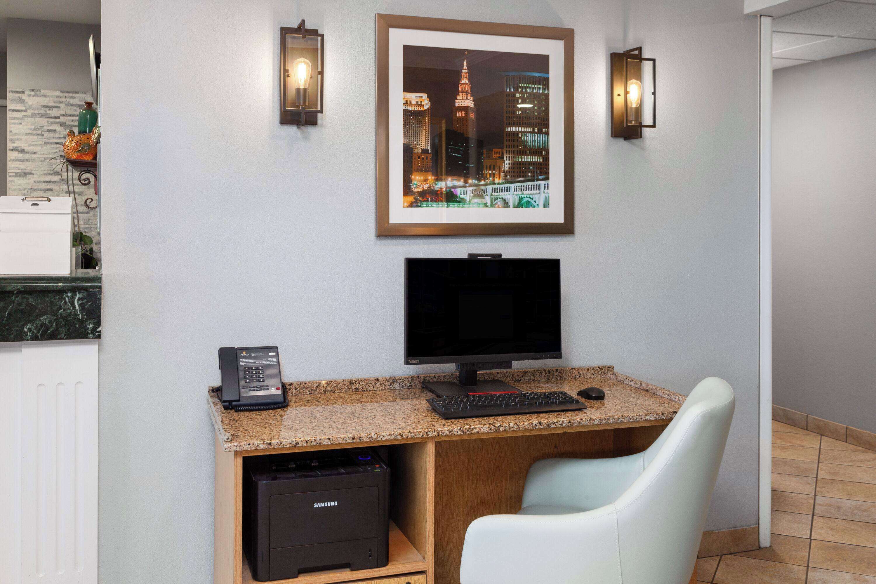 Habitación de hotel con escritorio, computadora, teléfono y una silla.