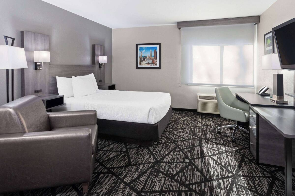 A hotel room with a large bed, a desk, a chair, a TV, and a picture on the wall.