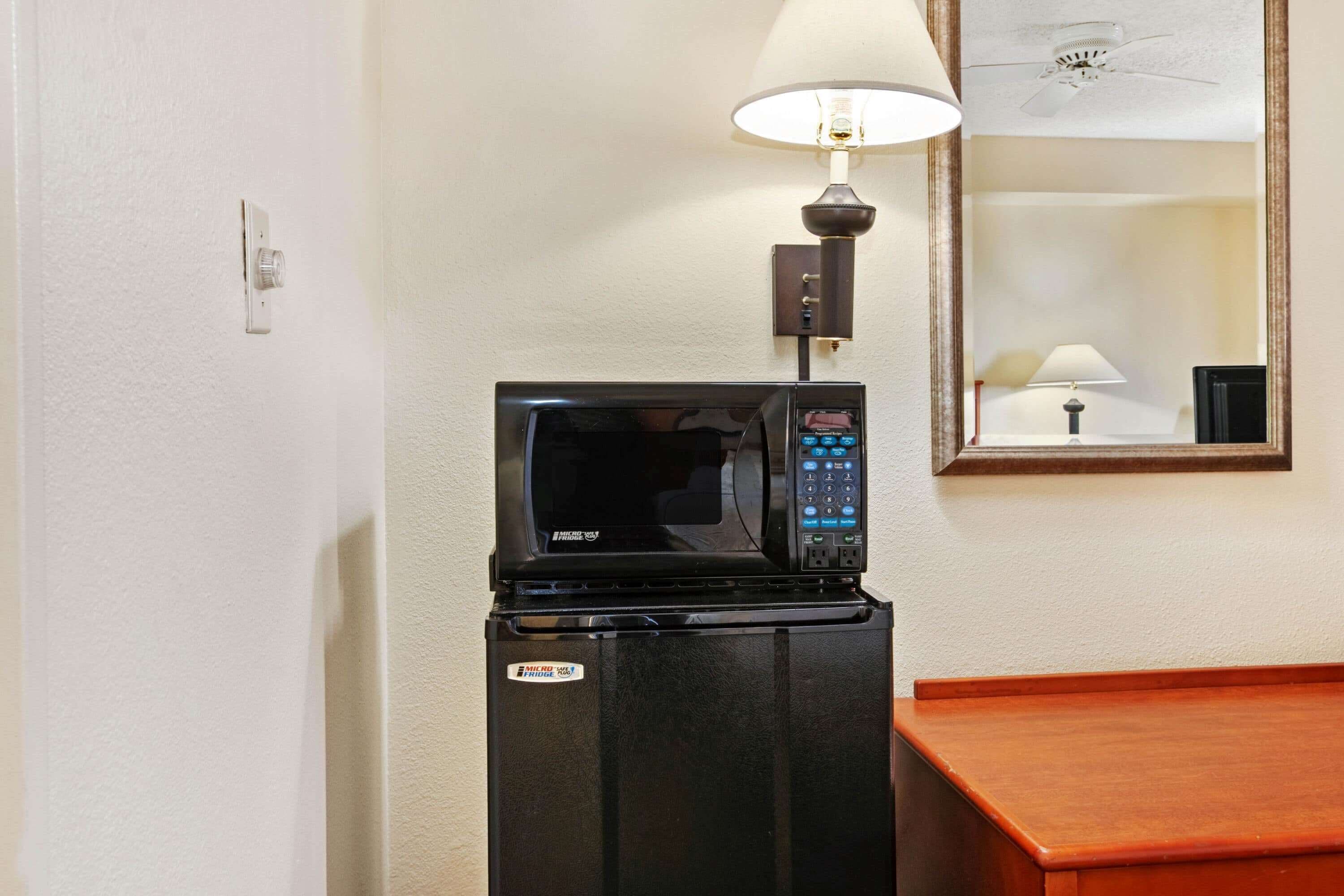 A compact microwave on a black refrigerator in a hotel room.