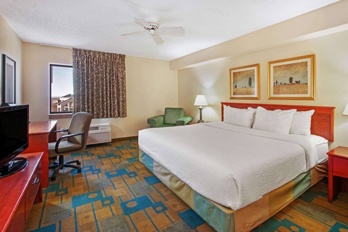 A hotel room with a bed, desk, chair, television, and two paintings on the wall.