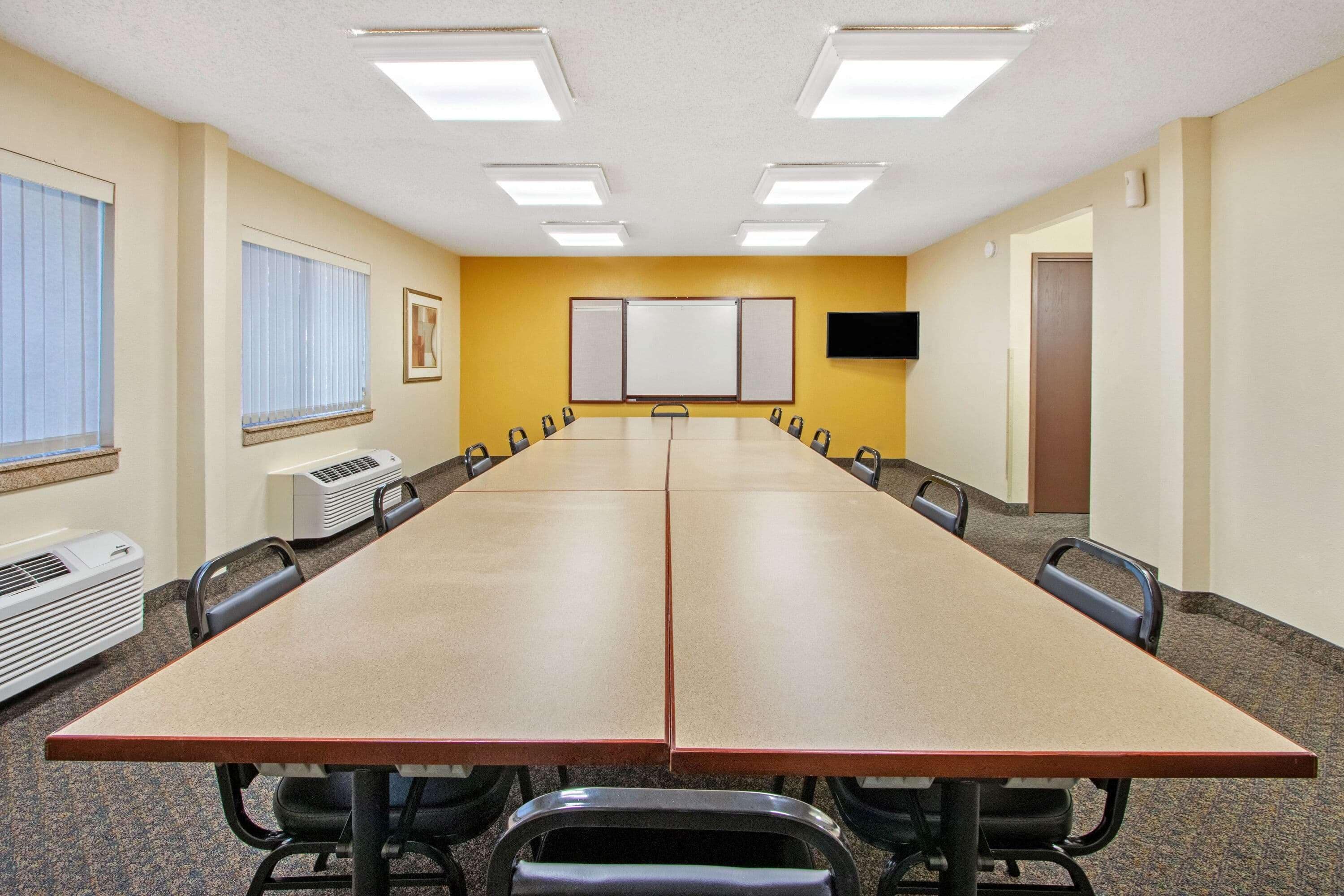 Une salle de conférence équipée d’une longue table, de chaises, de climatiseurs, d’un tableau blanc et d’un téléviseur fixé au mur.