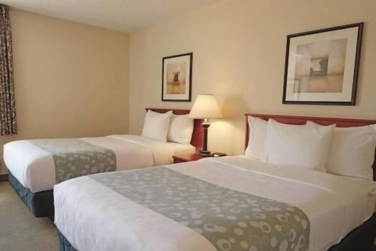 A hotel room with two beds, a nightstand, a lamp, and framed pictures on the wall.