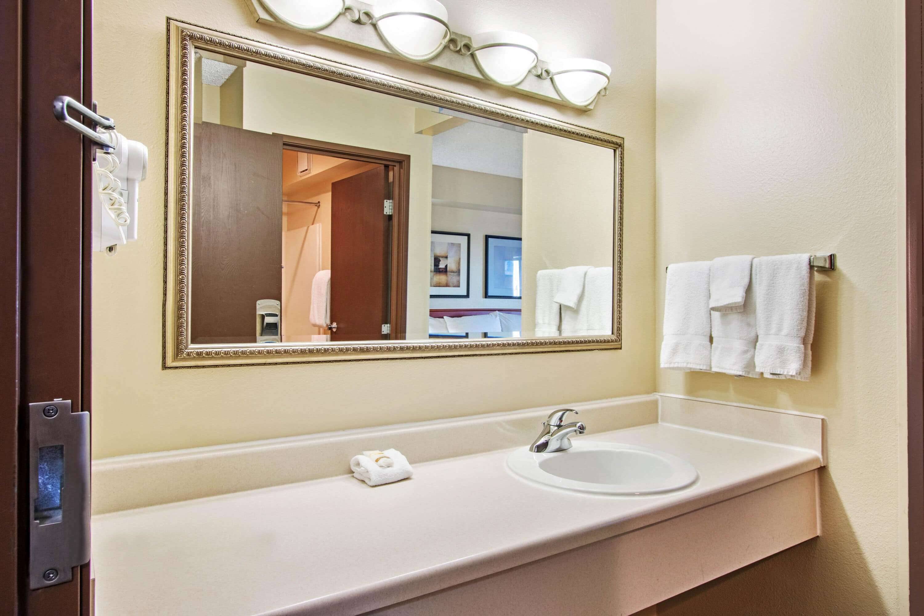 A hotel bathroom with a large mirror, a sink, and a towel rack.