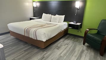 A hotel room with a bed, a nightstand, a green wall, and a green chair.