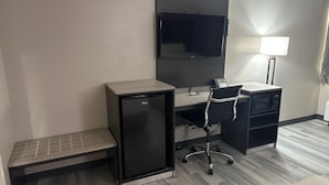 Habitación de hotel pequeña con kitchenette, un escritorio, una silla, televisión de pantalla plana y una lámpara.