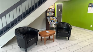 Un vestíbulo con una escalera, dos sillones de cuero negro, una mesa de madera y una pared verde con un cartel.