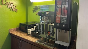 Una estación de café con una máquina de espresso Bunn, una cafetera y un letrero que anuncia zumo 100% naranja y manzana.