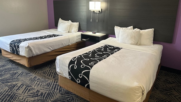 Una habitación de hotel con dos camas, una mesita de noche y una lámpara fijada a la pared.