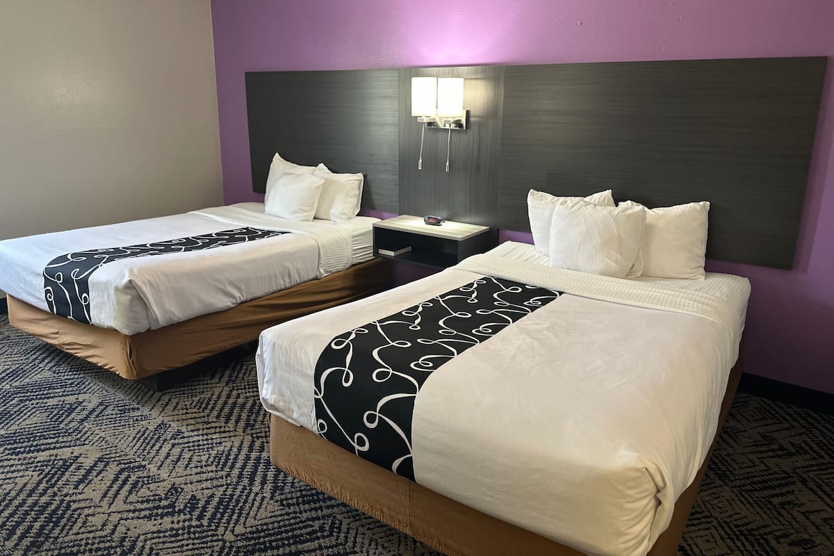 A hotel room with two beds, a nightstand, and a wall-mounted lamp.