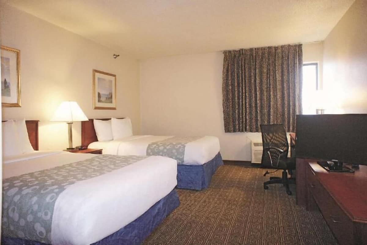 A hotel room with two beds, a desk, a chair, a TV, and a window with curtains.
