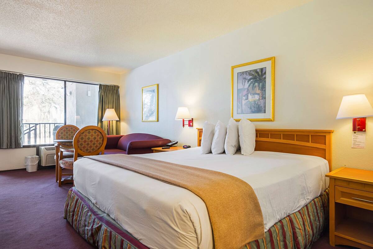 A hotel room with a large bed, a chair, a small table, a lamp, and a picture on the wall.