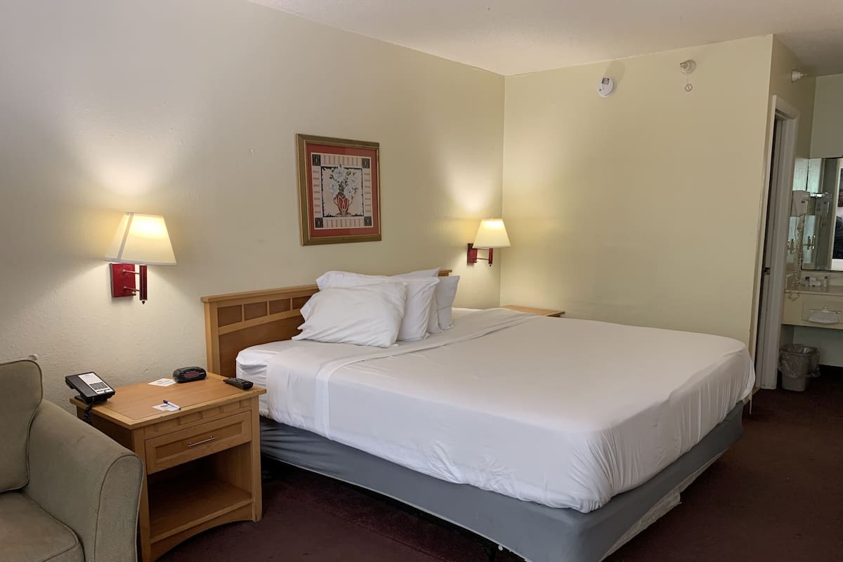 A hotel room with a bed, bedside lamps, a desk with a phone, a chair, and a wall-mounted picture.