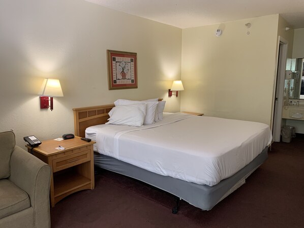 A hotel room with a bed, bedside lamps, a desk with a phone, a chair, and a wall-mounted picture. - Americas Best Value Inn & Suites Melbourne (Melbourne)
